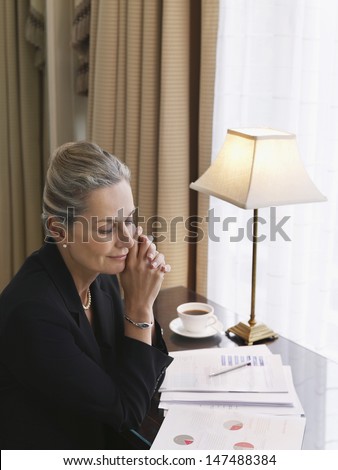 Middle aged businesswoman reading documents at home office desk