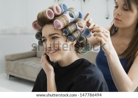 Happy Female model using cellphone while having her hair curled