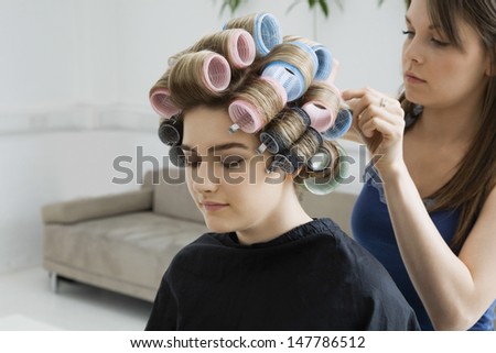View of a cropped stylist fixing rollers in female model\'s hair