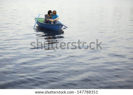Loving young couple cuddling in rowboat at lake