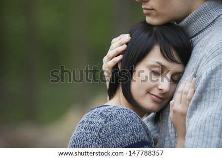 Closeup side view of a young woman laying head on man\'s chest against blurred background