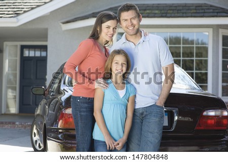 Portrait of a happy couple with daughter standing against car and house