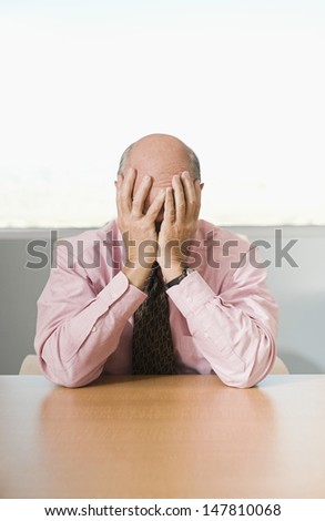Stressed businessman with head in hands sitting at office desk