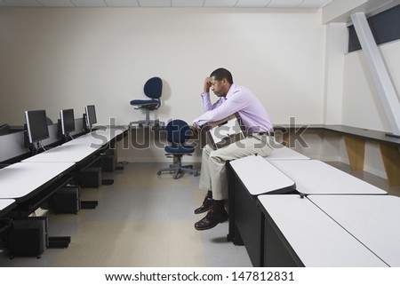 Full length side view of a depressed man sitting on desk with moving box