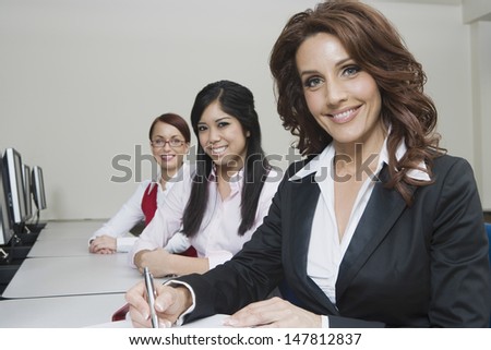 Portrait of three smiling multiethnic businesswomen sitting at office desk