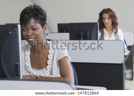 Smiling African American businesswoman working on computer with colleague in background