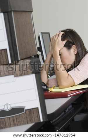 Side view of a stressed Asian businesswoman and moving boxes at office desk