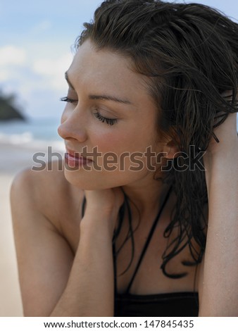 Closeup of a beautiful young woman with eyes closed and hands in hair at beach