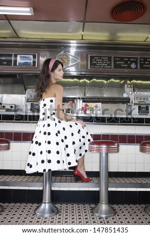 Full length side view of a young woman sitting at the diner counter