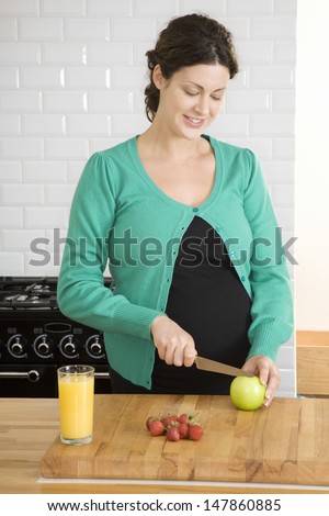 Pregnant young woman preparing cutting fruit in the kitchen at home