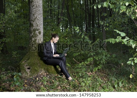 Full length side view of a young businesswoman using laptop in forest