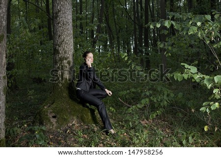 Full length side view of a young businesswoman using mobile phone in forest