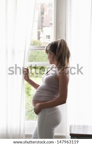Side view of young pregnant woman looking out of window