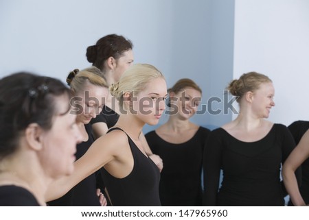 Serious young female ballet dancer with classmates in rehearsal room