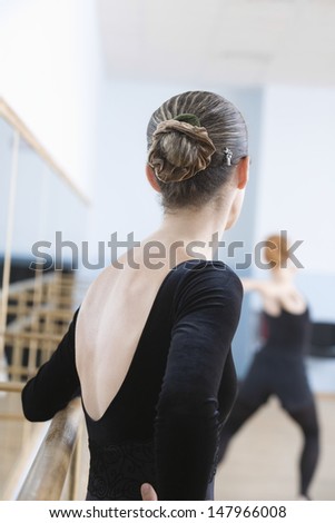 Rear view of young female ballet dancer standing by handrail in rehearsal room