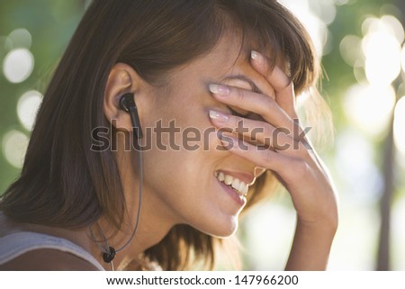 Side view of smiling young woman covering her face while listening to music in park