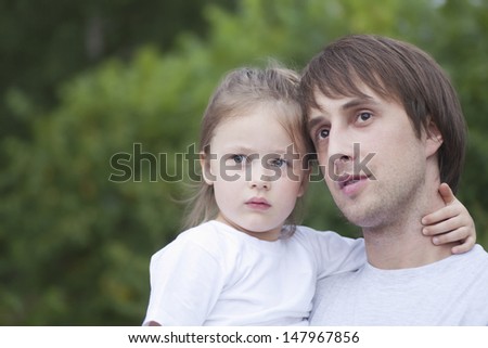 Closeup of father and daughter arm around looking away in park