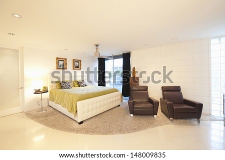Partly carpeted bedroom with matching leather armchairs in modern house