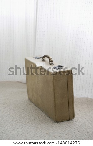 Old fashioned suitcase with tag by net curtains