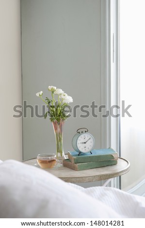 Bedside table with cut flower and alarm clock in bedroom