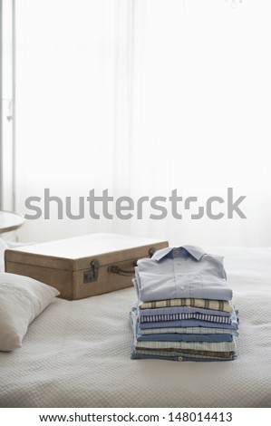 Ironed and folded shirts on bed next to suitcase in bedroom