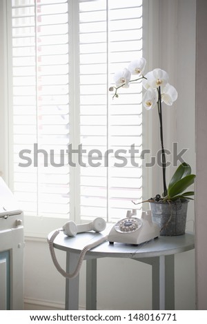 Rotary phone off the hook on a side table by shutter window