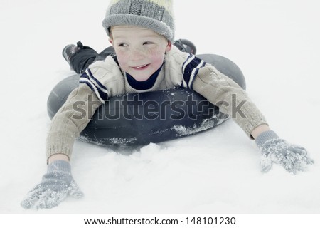 Happy young boy in winter clothing sledging on snow tube