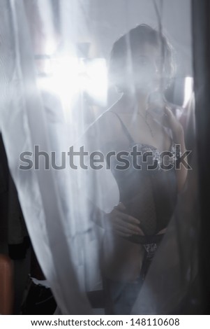 Sexy young woman in underwear behind curtain