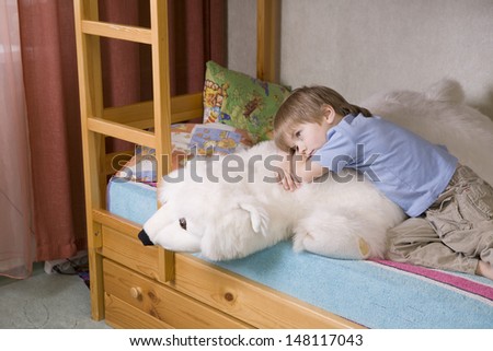 Thoughtful young boy with polar bear soft toy lying on bunk bed