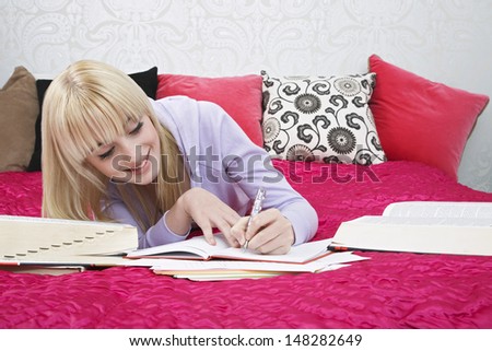 Beautiful teenage student writing in book while smiling on bed