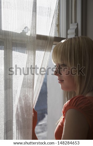 Beautiful teenage girl looking through window at home