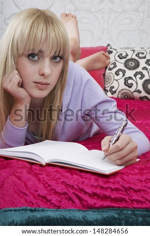Portrait of beautiful teenage girl writing in book on bed