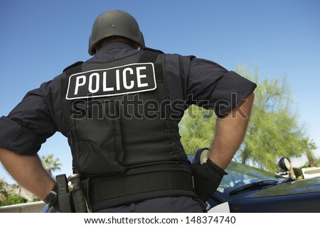 Rear view of policeman in uniform standing against car
