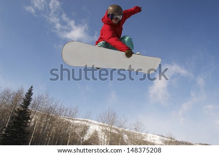 Low angle view of young male snowboarder jumping against sky