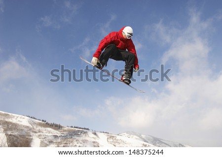 Low angle view of young male snowboarder jumping against cloudy sky