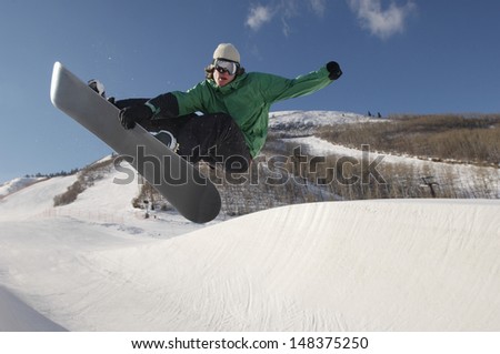 Full length of young snowboarder performing stunts on snowy hill