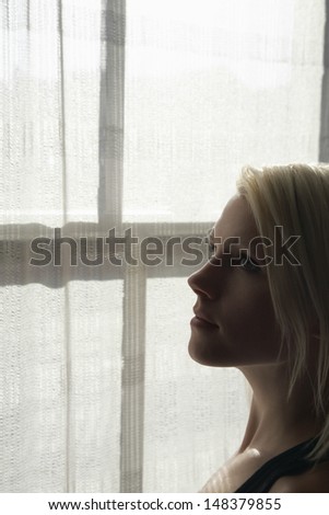 Closeup of thoughtful woman looking up against window in house