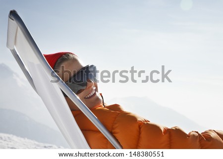 Happy woman in warm clothing relaxing on deck chair against sky