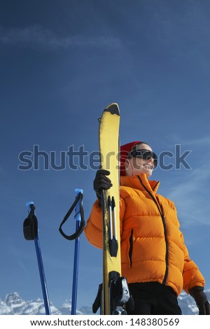 Low angle view of happy woman in winter jacket holding ski against blue sky