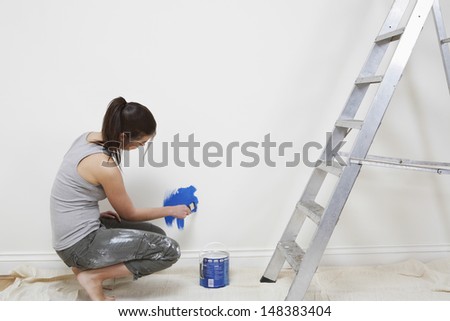 Side view of young woman painting wall with paintbrush at home