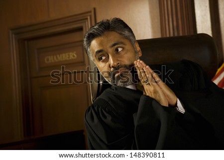 Thoughtful male judge with hands clasped looking away in court room