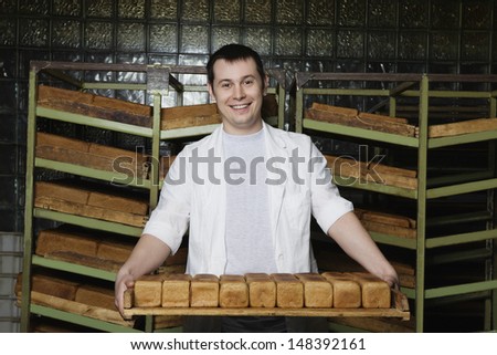Portrait of smiling young man carrying freshly baked breads in bakery