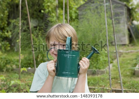 Portrait of happy young boy holding watering can in community garden