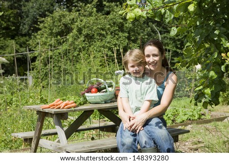 Portrait of happy mother and son with vegetables sitting on picnic table in allotment