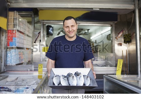 Portrait of confident owner displaying fresh fish in store