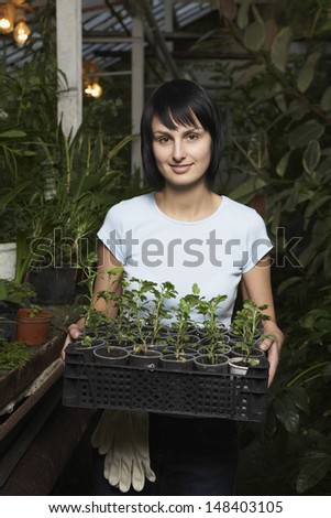 Portrait of young female botanist carrying potted plants in crate at greenhouse