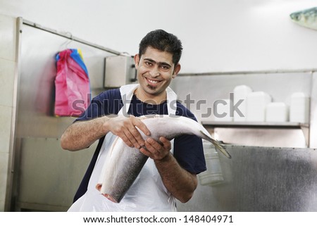 Portrait of happy young male butcher holding fish while sitting in store