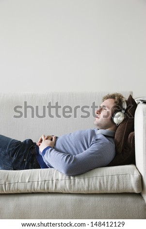 Side view of young man listening music while lying on sofa
