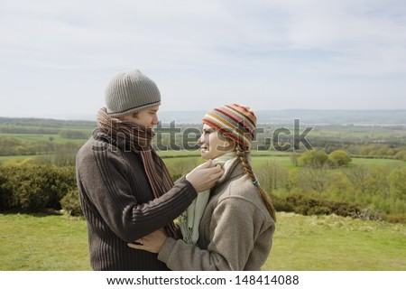 Side view of romantic young couple in warm clothing looking at each other in field