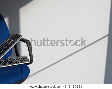 Closeup of two computer keyboards on office chair against wall